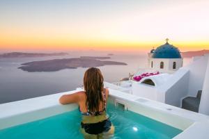 a woman sitting in a swimming pool looking out at the sunset at Cilon Suites Santorini in Imerovigli