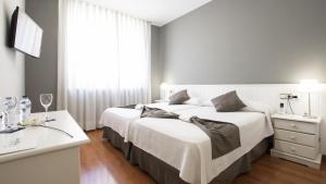 Un dormitorio con dos camas y una mesa y una ventana. en Hotel Isabel de Segura, en Teruel
