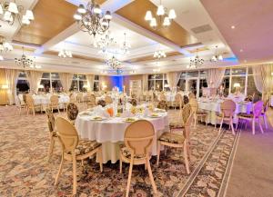 um salão de banquetes com mesas e cadeiras brancas em Hotel Lipowy Most em Supraśl