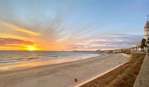 uma praia ao pôr do sol com um farol e o oceano em Mirador Playa Caleta Cádiz Centro Grupo AC Gestion em Cádis