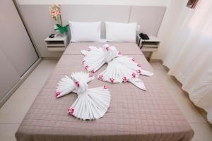 uma cama com lençóis brancos e flores em Flats Andira Kuss em Sinop