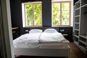 uma cama com lençóis brancos e almofadas num quarto com duas janelas em Hotel Restaurant Joseph em Bruckneudorf