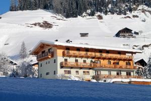 a large building in the snow with snow covered mountains at Ferienwohnungen Steidl in Innervillgraten