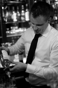 Un homme en cravate versant une bouteille de vin dans l'établissement Hotel Zee en Duin, à Katwijk