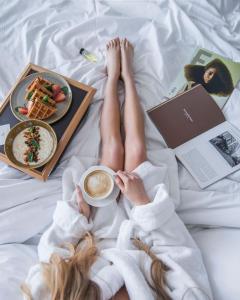 une femme qui se couche sur un lit avec une tasse de café et une assiette de nourriture dans l'établissement Four Elements Perm, à Perm