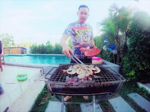 un hombre cocinando comida en una parrilla junto a una piscina en Cheap Pool Villa Hauhin (3 BR 1 Lounge) European Kitchen, en Hua Hin