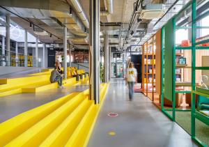 une bibliothèque avec des bancs jaunes et des personnes qui y marchent dans l'établissement The Social Hub Delft, à Delft