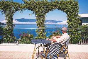 un hombre sentado en una mesa mirando hacia el agua en Carine Hotel Kumbor Superior en Herceg-Novi