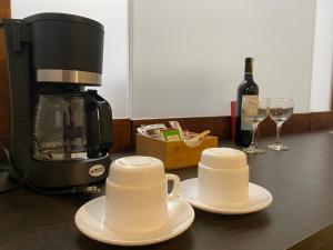 Zwei Tassen, eine Kaffeemaschine und Weingläser stehen auf der Theke. in der Unterkunft Galapagos Sunset Hotel in Puerto Baquerizo Moreno