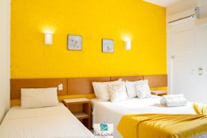 two beds in a room with a yellow wall at Pousada Dom Capudi in Bombinhas