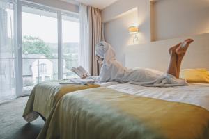 a woman laying on a bed reading a book at Holimo Hotel in Stronie Śląskie