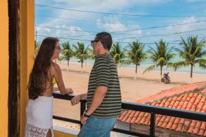 a man and woman standing on a balcony looking at the beach at Pousada Praia Dos Encantos in Japaratinga