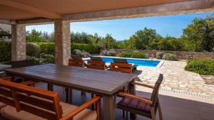 a wooden table and chairs on a patio with a swimming pool at More More Villa 4 All in Linardići
