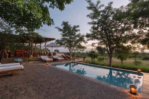 a swimming pool with a patio and trees in the background at Baobab Ridge in Klaserie Private Nature Reserve