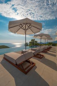 eine Reihe von Liegestühlen mit Sonnenschirmen auf einer Terrasse in der Unterkunft Vivid Blue Serenity Resort in Sveti Stefan