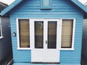 ein blaues Haus mit einer weißen Tür und Fenstern in der Unterkunft Stargazing Beach Hut on Mudeford Sandbank with wake up sea views in Christchurch