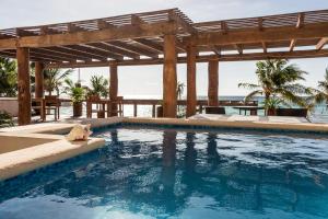 una piscina con pérgola de madera y el océano en Aquastar Hotel & Apartments en Mahahual