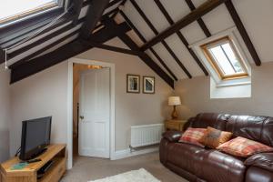 a living room with a leather couch and a tv at Cliff House Holiday Cottages in Ebberston