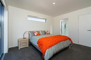 a bedroom with a bed with an orange blanket at Dune Views - Mangawhai Heads Holiday Home in Mangawhai