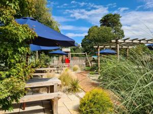 un jardín con bancos de madera y sombrillas azules en The Red Lion, en Kilsby