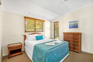 a bedroom with a bed with a blue blanket and a dresser at Tin Can Bay Marina Villas in Tin Can Bay