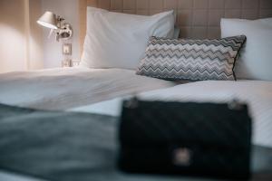 1 cama con sábanas y almohadas blancas y una maleta negra en Domotel Olympia en Tesalónica