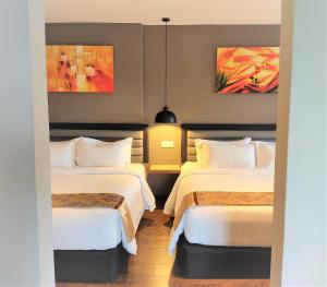 two beds in a room with two paintings on the wall at Apple Suites Hotel in Sitiawan