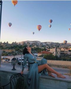 a woman sitting on a ledge looking up at hot air balloons at Caravanserai Inn Hotel in Göreme