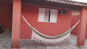 a hammock on the side of a red house at Casa com ar condicionado e 2 suítes ilha comprida in Ilha Comprida