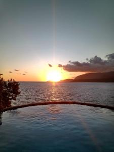 una puesta de sol sobre un cuerpo de agua con una piscina en Magnífica Costeira, en Ilhabela