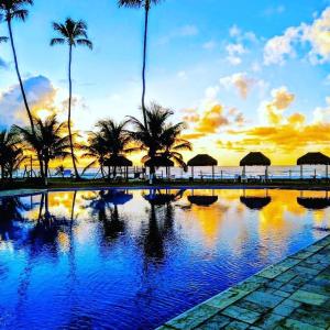 a swimming pool with palm trees and the ocean at sunset at Ancorar Resort em Porto de Galinhas in Porto De Galinhas