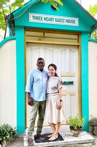 a man and a woman standing in front of a three heart guest house at Three Hearts in Fulhadhoo