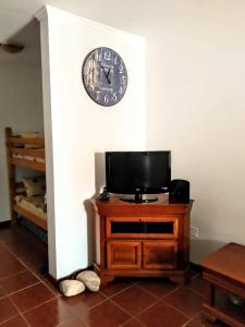 a clock on a wall above a television on a cabinet at Refugio das Matas in Porto Santo