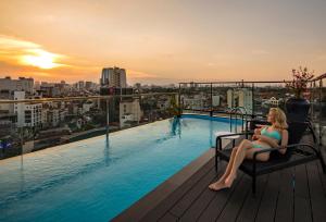 a woman sitting on a chair next to a swimming pool at Soleil Boutique Hotel Hanoi in Hanoi