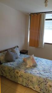 1 dormitorio con 1 cama con colcha de flores y ventana en Kitnet Aurora, en Miguel Pereira