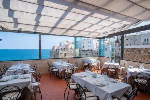 un restaurant avec des tables et des chaises blanches et l'océan dans l'établissement Covo dei Saraceni, à Polignano a Mare