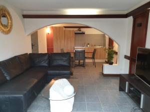 a living room with a black leather couch and a kitchen at Ty Keramor in Hôpital-Camfrout