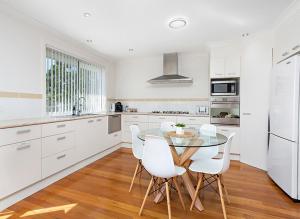 a white kitchen with a glass table and white chairs at kims@kiama in Kiama