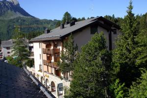 a building on a hill with trees and a mountain at Hotel Pöstli in Maloja