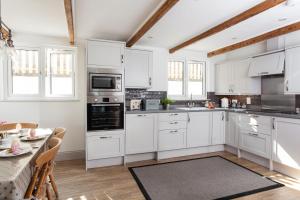 a white kitchen with white cabinets and a table at Trevarrow Cottage in Coverack