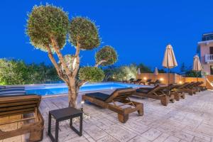 a pool with benches and a tree next to a building at Litore Luxury Living in Laganas