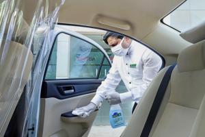 a man wearing a mask and gloves cleaning the door of a car at Lazy Lagoon, Baga A Lemon Tree Resort, Goa in Baga