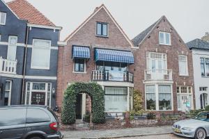 a red brick house with an arbor and cars parked in front at B&B de Zandtaart in Egmond aan Zee