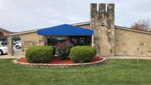 a building with a blue awning and two bushes at FairBridge Inn Express Merrillville in Merrillville