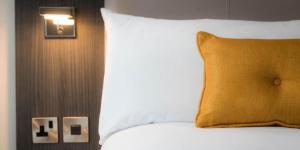 a white bed sitting under a lamp next to a wall at Maldron Hotel Belfast International Airport in Aldergrove