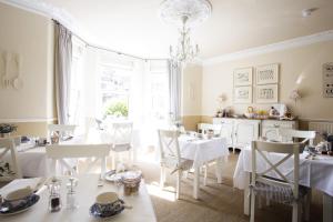 una sala da pranzo con tavoli e sedie bianchi e un lampadario a braccio di Brindleys a Bath