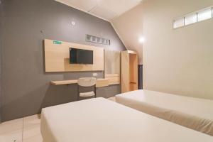 a room with two beds and a desk and a tv at RedDoorz At Hotel Arimbi Dewi Sartika Baru in Bandung