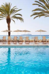 a swimming pool with chairs and umbrellas and the ocean at Grupotel Imperio Playa in Sant Joan de Labritja