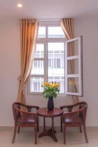 d'une table, de deux chaises et d'une fenêtre avec un vase de fleurs. dans l'établissement Dalat Joy Hotel, à Đà Lạt