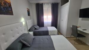 Habitación de hotel con 2 camas y escritorio en Hostal Málaga en Arcos de la Frontera